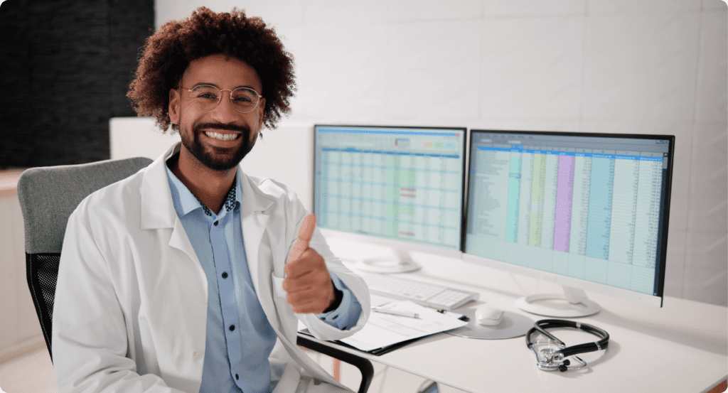 Medical coder giving a thumbs up in front of dual monitors